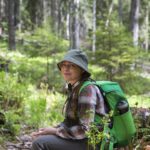 Retkeilijä istuu hymyillen reppu selässään maassa keskellä metsää. Kuva: Saara Lavi