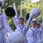 Close-up of girls dressed in white nautical dresses, performing at Maritime festival parade. Girls are holding white and dark blue pompoms.