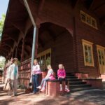 Keisarillinen kalastusmajan edustalla kaksi aikuista ja kaksi istuvaa lasta. Kuva: Elias Lahtinen.