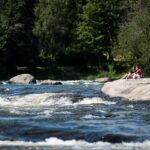 Kaksi ihmistä istuu kalliolla. Etualalla vuolaana virtaava Langinkoski: Kuva: Elias Lahtinen
