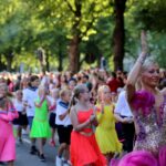 Close-up of Maritime festival parade. A woman and younger girls wearing bright dresses and clapping their hands.