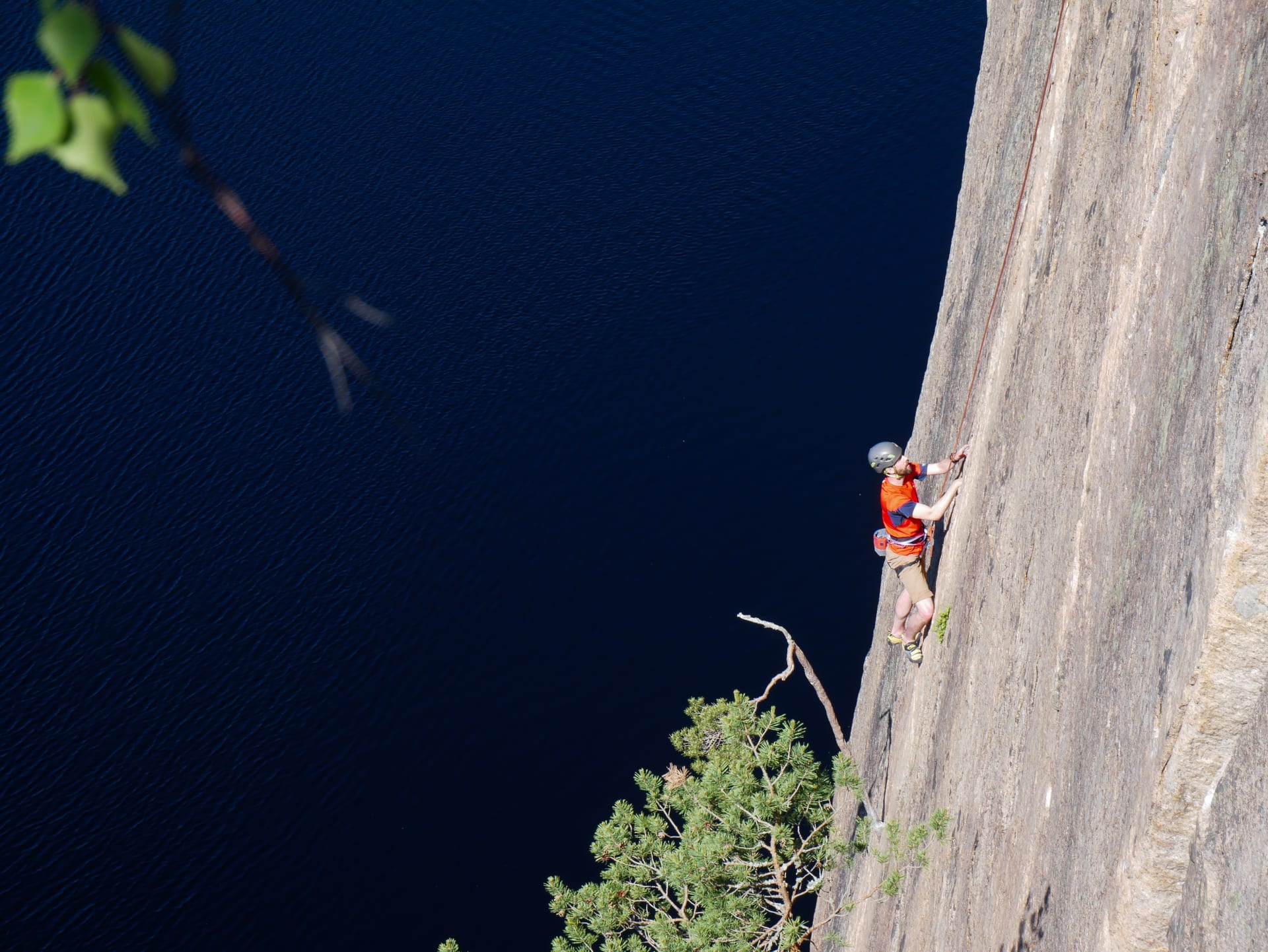 Kiipeilijä nousemassa Olhavan kiipeilykalliolla lammen yläpuolella.