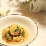 A dish of pike and crab broth is served on a golden-edged plate.