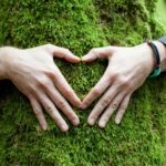 Hands hugging a mossy tree and formin a heart