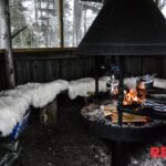 Open hut with a campfire in the middle and kettles cooking on the fire.